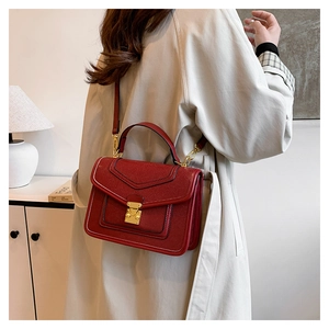 Detail of red lizard-embossed shoulder bag featuring a golden triangular push-lock buckle
