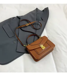 Detailed view of brown litchi grain leather handbag with gold metal lock and shoulder strap