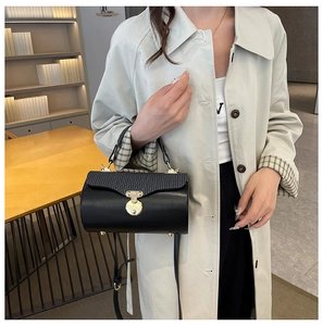 Detail of black cylindrical box bag with textured flap, golden hardware and shoulder strap