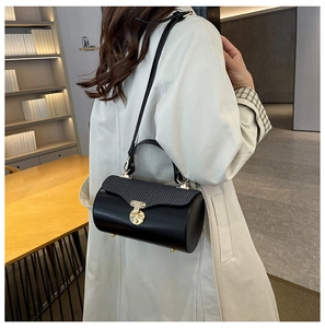 Detail of black leather cylindrical handbag featuring pleated flap and gold metal clasp