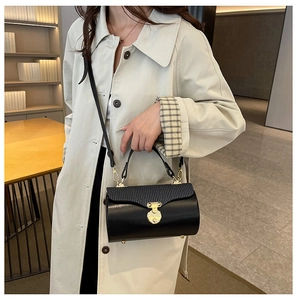 Detail of a chic black cylindrical crossbody bag with gold hardware on a beige coat