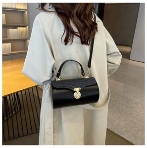 Detail of a black cylindrical crossbody bag featuring exotic leather texture and gold hardware