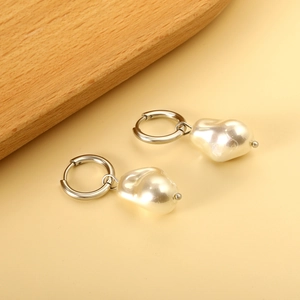Close-up of Baroque pearl earrings with silver metallic hoops on a warm beige background