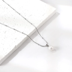 Detail of a white freshwater pearl pendant on a beaded silver-tone snake chain necklace