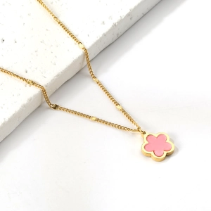 Dettaglio della collana dorata con ciondolo a fiore rosa su sfondo di pietra bianca