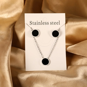 Elegant stainless steel jewelry set featuring black circular pendants on gold silk background