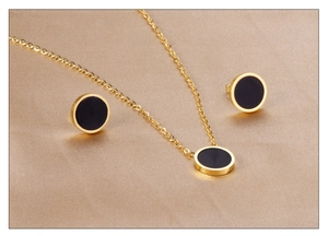 Detailed close-up of golden necklace and earrings set with black shell inlays on silk