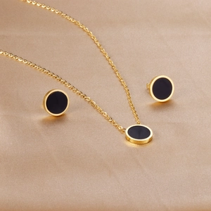 Elegant gold necklace and black shell earring set on champagne silk fabric background