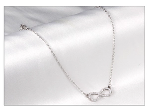 Close-up of infinity pendant with white zircon crystals on smooth white silk