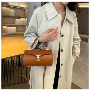 Close-up of brown leather cylinder bag featuring elegant wave-textured flap and gold lock