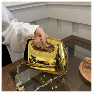 Detail of glossy gold crescent handbag with hollow handle and detachable chain strap