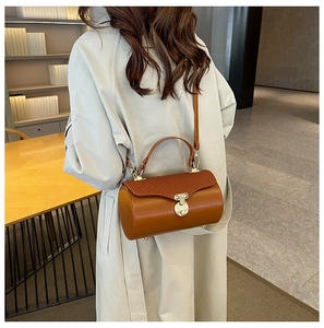 Detail of a brown cylindrical crossbody bag with gold hardware and wavy textured flap