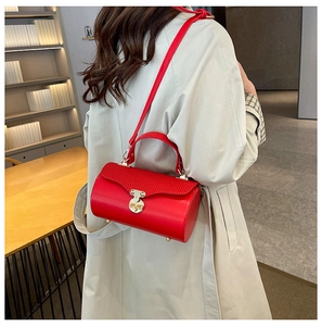 Detail of red cylindrical crossbody bag showing wavy embossed flap and gold metal clasp