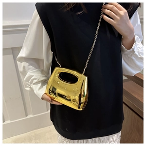 Detailed view of a gold metallic sculptural handbag with fine gold chain strap