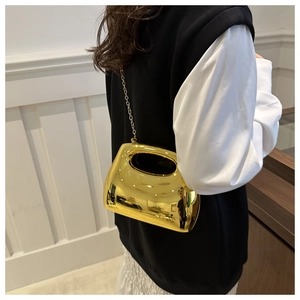 Detail of a minimalist gold mirrored metal handbag with a sleek oval cutout handle