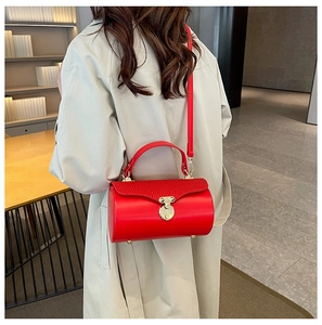 Red leather cylinder bag with gold clasp shown on model wearing beige trench coat