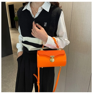 Close-up of vibrant orange cylinder bag with wave embossed texture and gold buckle