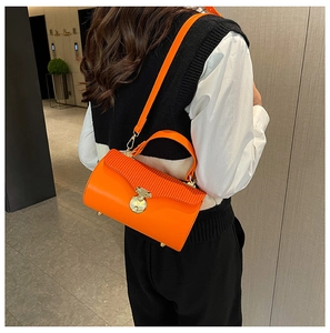 Detail of bright orange box bag with pleated flap and golden twist lock on a shoulder strap