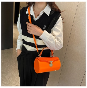 Close-up of orange leather cylinder box bag with gold lock and adjustable strap