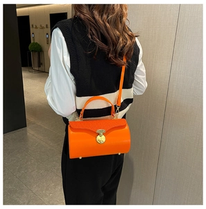Detail of a bright orange cylindrical box bag featuring golden round clasp and leather texture