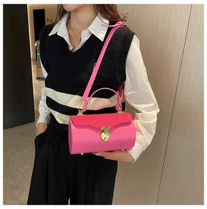 Pink cylinder handbag with pleated flap and gold lock shown on model as a shoulder bag