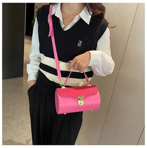 Detail of bright pink cylindrical handbag featuring gold metal disc closure and pleated top