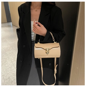 Detail of beige cylindrical box bag featuring wavy pleated flap and gold metal twist lock