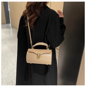 Detailed view of cream cylindrical box bag with textured lid and gold circular lock
