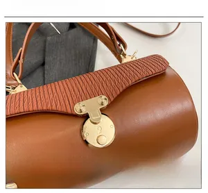 Detail of a brown leather box bag featuring a pleated flap and golden circular metal lock