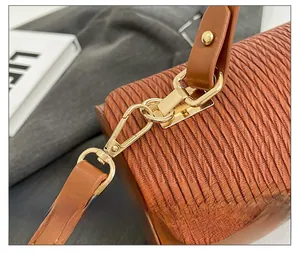 Close-up of golden metal clasp and vertical pleated texture on brown crossbody bag