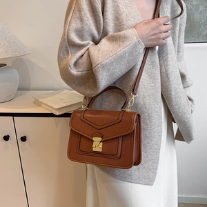 Brown lychee leather crossbody bag with gold lock buckle on a beige knit dress