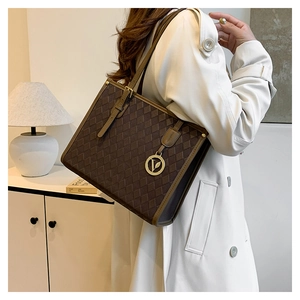 Detail of dark brown tote bag with quilted pattern and metal logo charm on a model