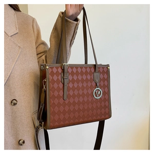Detail of a brown quilted tote bag with a V-shaped metal pendant and luxury texture