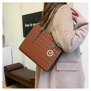 Detail of checkered tote bag featuring leather texture and golden V pendant charm