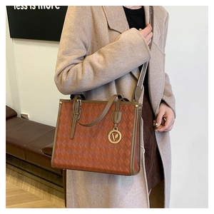 Detail of vintage brown tote bag featuring quilted texture and a gold V-shaped charm