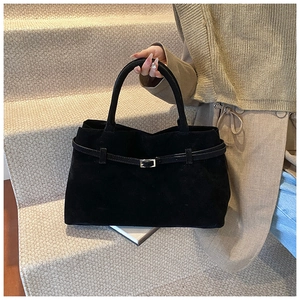 Detail of matte black tote bag featuring decorative belt buckle and suede texture