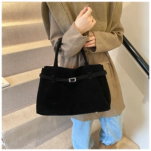 Detail of black suede tote bag featuring silver metal buckle and protective bottom feet