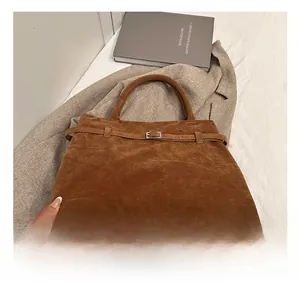 Detail view of brown faux suede tote bag with decorative metal buckle and bottom rivets