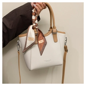 Détail d'un sac seau en cuir beige avec un foulard en soie décoratif sur la poignée