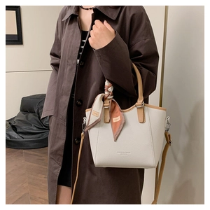Détail d'un sac seau crème avec poignée en cuir marron et foulard floral décoratif