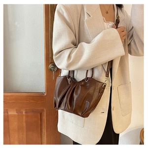 Gros plan du sac seau plissé marron avec bandoulière réglable et détails dorés