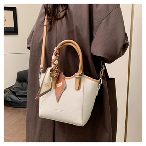 Détail d'un sac seau blanc crème avec poignée caramel et foulard en soie sur un manteau