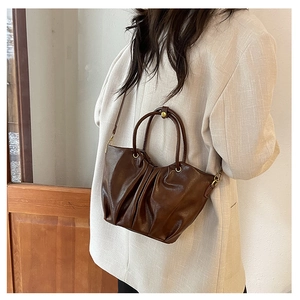 Détail du sac plissé en cuir marron foncé avec anneaux dorés et bandoulière longue