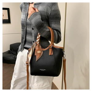 Détail d'un sac seau en cuir noir grainé avec poignées marron et foulard en soie décoratif