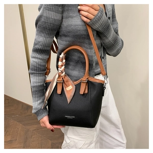 Détail du sac seau noir en cuir avec un foulard en soie sur la poignée marron