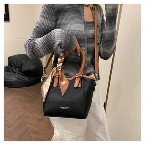 Détail d'un sac seau en cuir grainé noir avec poignée marron et foulard en soie à motif