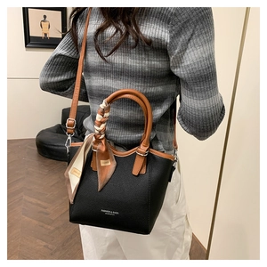 Détail du sac seau noir en cuir avec poignée marron enveloppée d'un foulard en soie