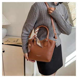 Sac seau en cuir marron avec foulard décoratif et bandoulière réglable porté par un mannequin