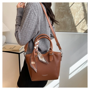 Sac seau en cuir marron avec foulard décoratif porté par un mannequin dans une pièce