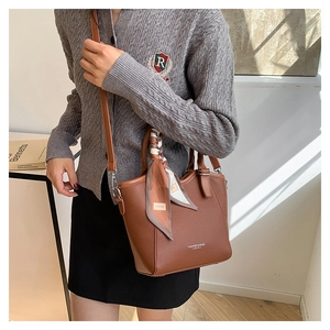 Détail du sac seau en cuir marron foncé avec texture litchi et foulard en soie au manche